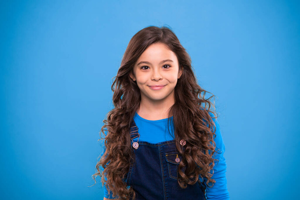 Extreme hair volume. Kid girl long healthy shiny hair. Little girl grow long hair. Teaching healthy hair care habits. Kid happy cute face with adorable curly hairstyle stand over blue background - Φωτογραφία, εικόνα