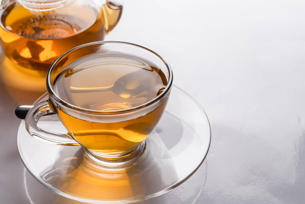 Primer plano una taza de té caliente recién hecho en vidrio transparente y tetera en la mesa con reflejo. - Foto, imagen