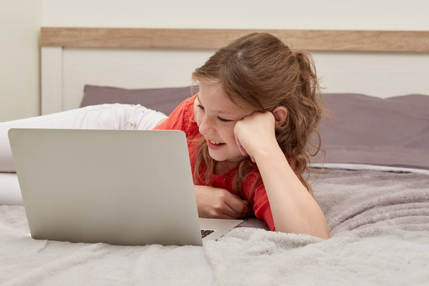 Cheerful positive girl watching cartoon lying in bed. - Photo, Image