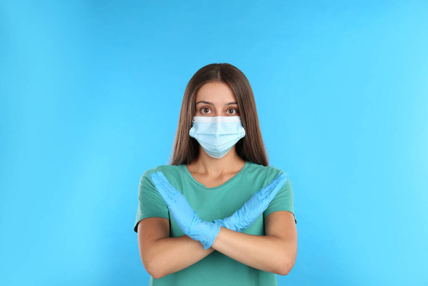 Woman in protective mask showing stop gesture on light blue background. Prevent spreading of COVID?19 - Foto, immagini