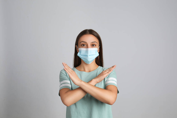 Woman in protective mask showing stop gesture on grey background. Prevent spreading of COVID?19 - Fotó, kép