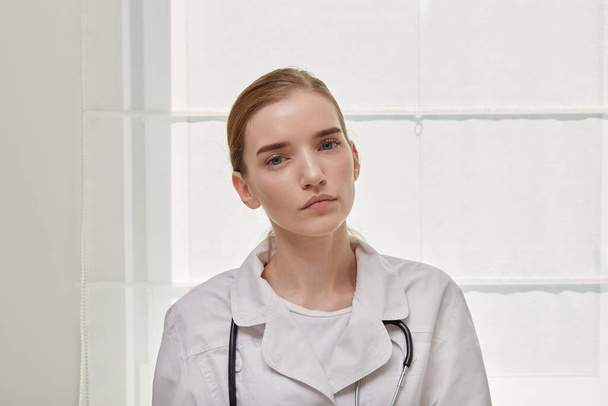 Portrait of a young beautiful confident woman doctor in a medical gown. - Фото, изображение