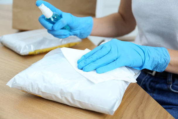 Woman cleaning parcel with wet wipe and antibacterial spray at wooden table, closeup. Preventive measure during COVID-19 pandemic - Zdjęcie, obraz