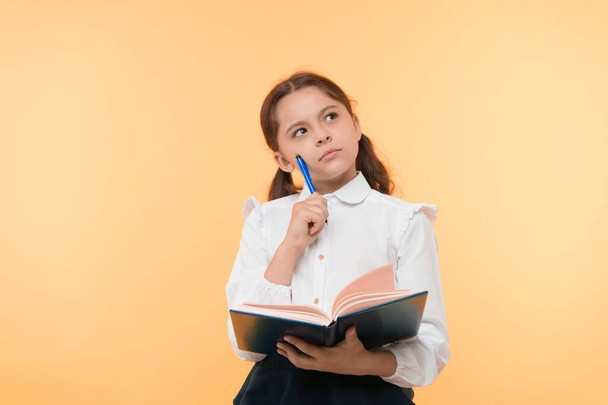 Girl cute schoolgirl in uniform hold book or textbook yellow background. Diligent pupil get knowledge from book. Child wear school uniform prepare for lesson her knowledge. Complex knowledge - Fotó, kép