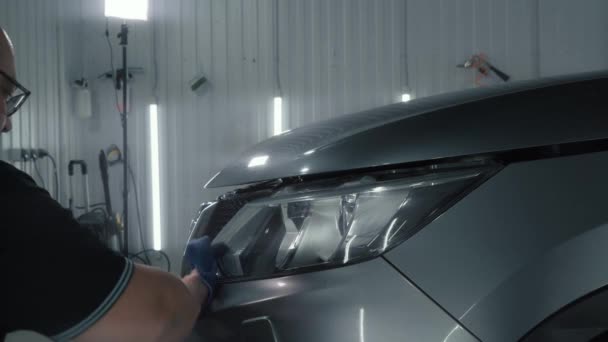 Detailing studio worker puffs cleaner on headlight and wipes it with microfiber, προετοιμασία προβολέων για γυάλισμα και αποκατάσταση - Πλάνα, βίντεο