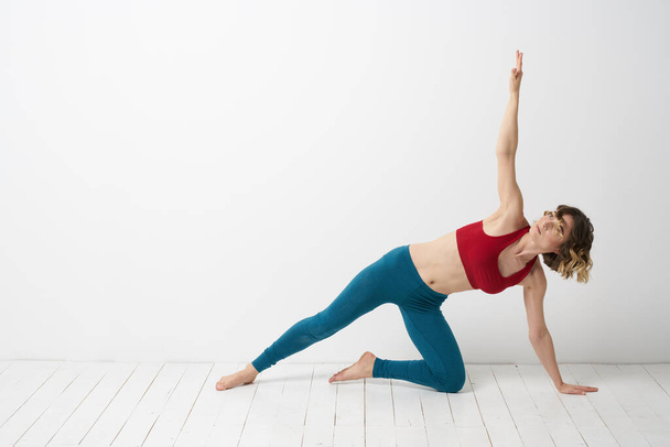 Eine Frau in blauen Jeans praktiziert Yoga vor hellem Hintergrund drinnen und eine schlanke Figur beim Turnen - Foto, Bild