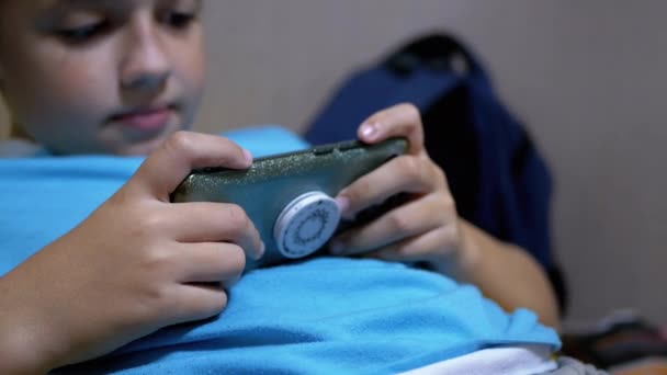 Uśmiechnięty chłopiec gra w grę mobilną na smartfonie w domu w zrelaksowanym stanie - Materiał filmowy, wideo