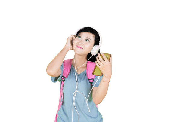 Female student enjoying music by using a headset while standing in the studio. Isolated on white background - Foto, Imagem