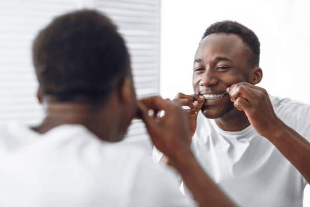 Toothy Αφρικής άνθρωπος Flosing δόντια χρησιμοποιώντας Floss στέκεται στο μπάνιο - Φωτογραφία, εικόνα