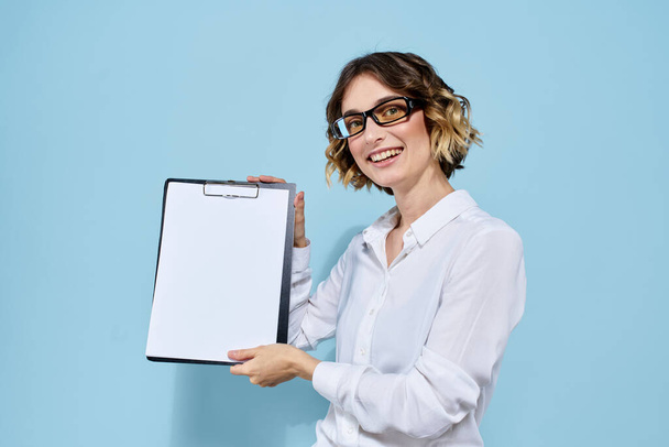 Bizneswoman z dokumentami w folderze na niebieskim tle i w jasnych okularach na twarzy - Zdjęcie, obraz