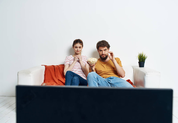 Bir adam ve bir kadın TV 'nin önündeki kanepede oturuyorlar ve yeşil bir çiçek evin içinde. - Fotoğraf, Görsel