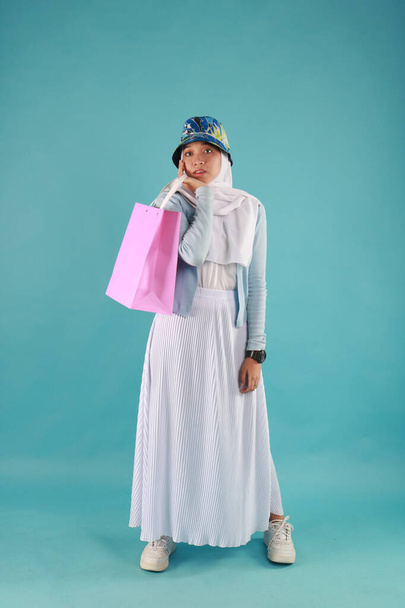 Portrait d'une belle fille excitée portant une robe tenant des sacs à provisions isolés sur fond bleu. - Photo, image