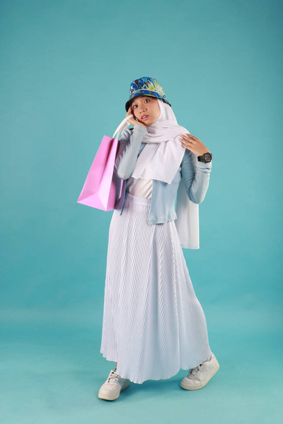 Portret van een opgewonden mooi meisje dragen jurk houden boodschappentassen geïsoleerd over blauwe achtergrond. - Foto, afbeelding