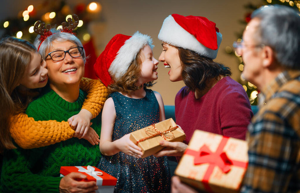 Mutlu Noeller ve mutlu tatiller! Büyükanne, büyükbaba, anne ve çocuklar hediye değiş tokuşu yapıyor. Ebeveynler ve kızlar kapalı alanda eğleniyorlar. Odasında hediyeler olan sevgi dolu bir aile. - Fotoğraf, Görsel