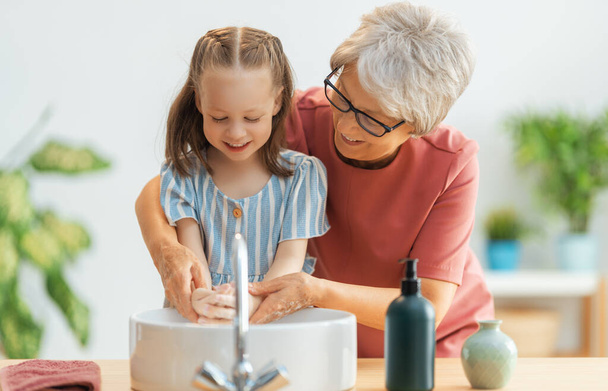 A cute little girl and her grandmother are washing their hands. Protection against infections and viruses.   - Foto, afbeelding
