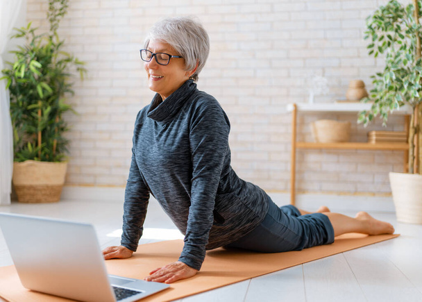 Senior woman in activewear watching online courses on laptop while exercising at home. - 写真・画像