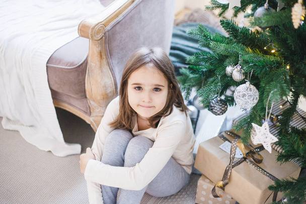 room is decorated for the new year, the girl is sitting near the Christmas tree, gifts, waiting for Christmas, home comfort - Foto, Imagem