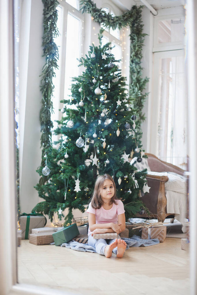 The room is decorated for the new year, the sister girls are sitting near the Christmas tree, giving gifts, waiting for guests - Foto, imagen