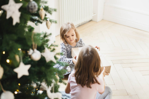 The room is decorated for the new year, the sister girls are sitting near the Christmas tree, giving gifts, waiting for guests - Valokuva, kuva