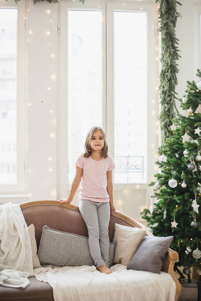 The room is decorated for the new year, a girl on the couch waiting for gifts, Christmas morning - Foto, Imagen