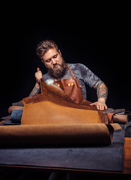 Skinner bearbeitet Leder mit Bastelwerkzeugen am Arbeitsplatz - Foto, Bild