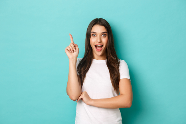 Image of pretty excited caucasian girl, having an idea, saying suggestion with finger raised up, standing in eureka pose over blue background - Photo, Image