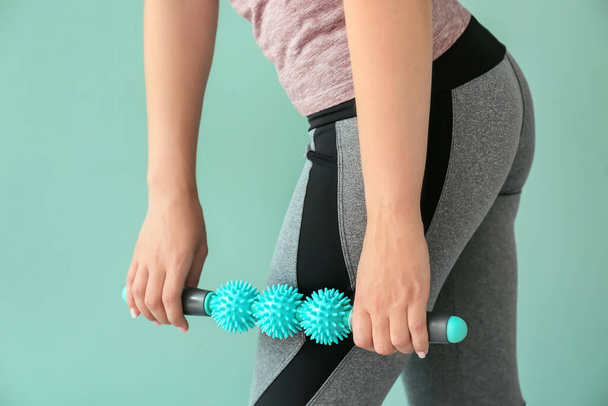 Sportswoman massaging herself with body roller on color background - Photo, Image