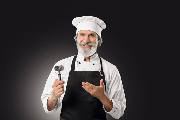 Ältere männliche Koch mit Pizzamesser auf dunklem Hintergrund - Foto, Bild