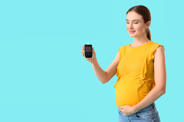 Pregnant diabetic woman with digital glucometer on color background - Foto, afbeelding