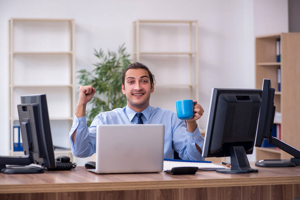 Young male employee drinking coffee in the office - Photo, Image