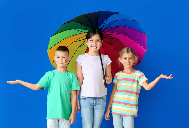 Niños pequeños con paraguas de arco iris sobre fondo de color - Foto, imagen
