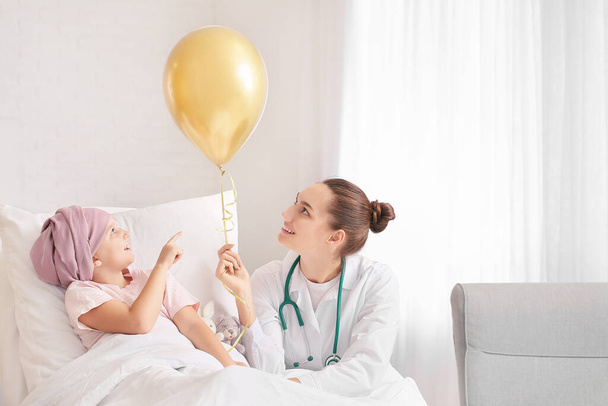 Lekarz ze złotym balonem i małą dziewczynką przechodzącą chemioterapię w klinice. Koncepcja świadomości na temat nowotworów u dzieci - Zdjęcie, obraz