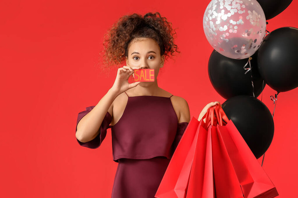 Beautiful African-American woman with shopping bags, credit card and balloons on color background. Black Friday sale - Zdjęcie, obraz