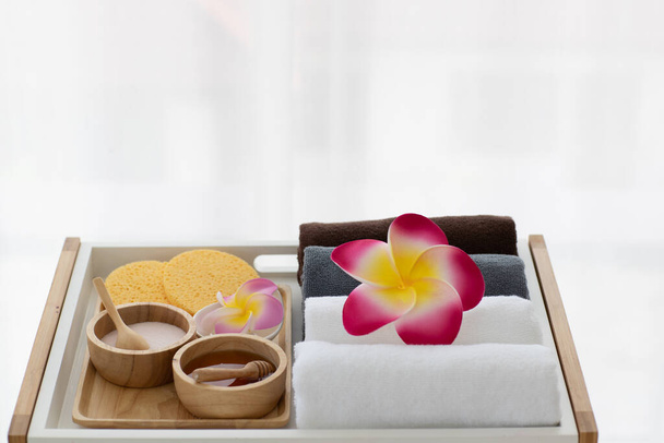 Set von Wellness-Behandlung Lamelle und Honig in einer hölzernen Schüssel mit Rollen sauberer Handtücher im Hintergrund mit bunten Plumeria Blume. - Foto, Bild