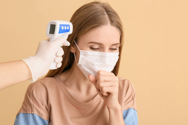 病気の女性と色の背景に赤外線温度計で手。コロナウイルスの流行 - 写真・画像