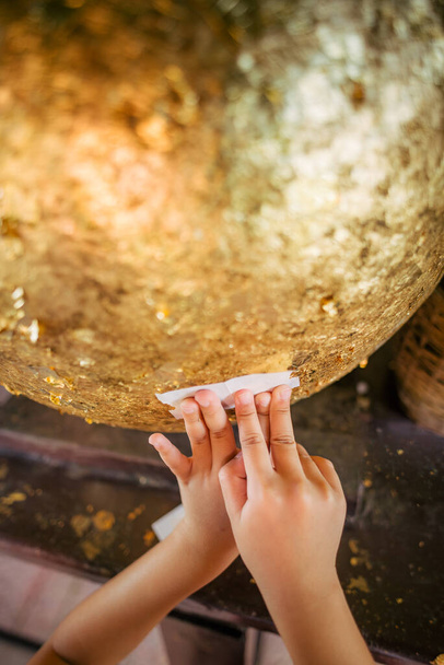 Un enfant essaie de coller une feuille d'or sur des pierres rondes enterrées que les Thaïlandais appellent "Luknimit", ce qui est une bénédiction selon les croyances religieuses. - Photo, image