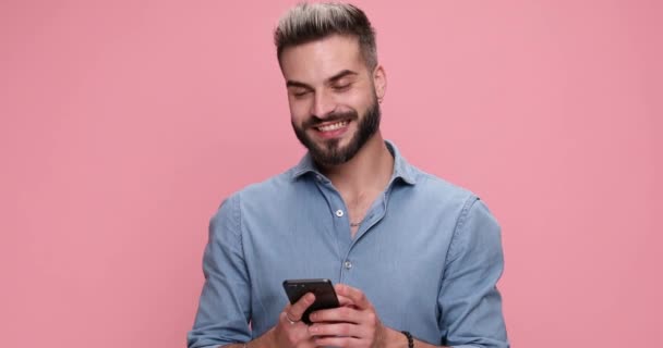 ležérní člověk psaní zprávy na svém telefonu a ukazuje na kameru na růžovém pozadí - Záběry, video
