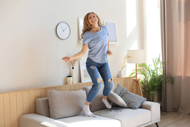 Приваблива молода жінка розважається вдома. Дівчина стрибає і танцює на дивані
 - Фото, зображення