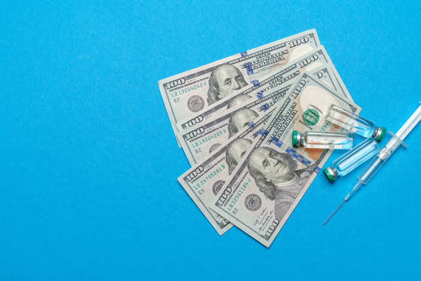 Close up 100 US dollar bills, syringe and vaccine ampoules over blue background - Fotografie, Obrázek