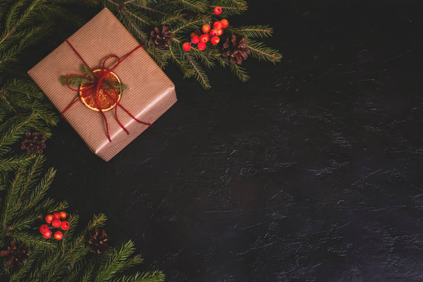 Χριστουγεννιάτικη σύνθεση. Χειροποίητο κουτί δώρου διακοσμημένο με χαρτί χειροτεχνίας με brunches σε σκούρο φόντο. Αντιγραφή χώρου - Φωτογραφία, εικόνα