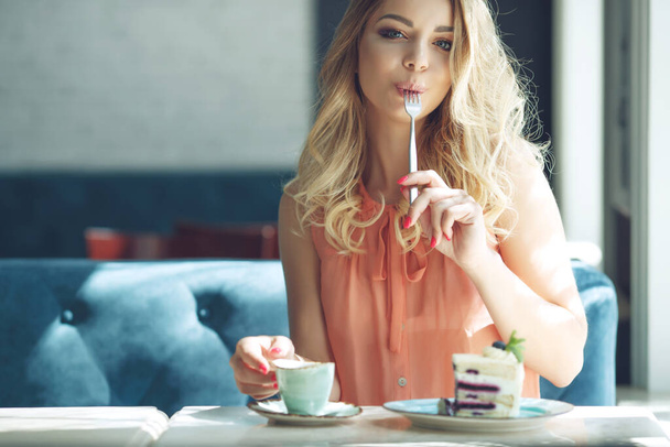 Молодая красивая женщина ест десерт. Веселая привлекательная молодая женщина с длинными волосами и поедающая десерт. - Фото, изображение