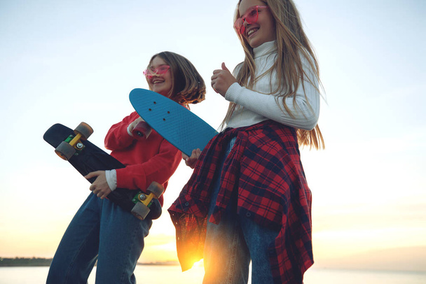 Twee vriendinnen spelen met skateboard skateboard in het park. Meisjes met een skateboard. Gelach en plezier. - Foto, afbeelding