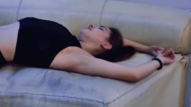 Egy gyönyörű sportasszony fekszik egy régi kanapén, nyújtózkodik és pihen edzés után.. - Felvétel, videó