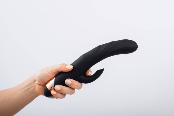 Faceless woman holding black dildo with clitoris stimulator on white background - Foto, afbeelding