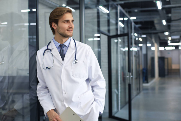 Portrait of doctor standing in hospital corridor wearing lab coat and stethoscope - Foto, imagen