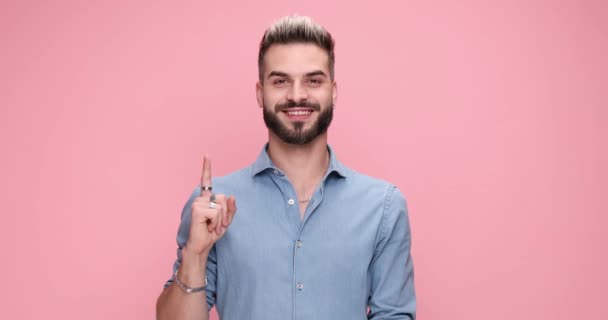 sorrindo homem casual apresentando seu dedo indicador para a câmera contra fundo rosa - Filmagem, Vídeo