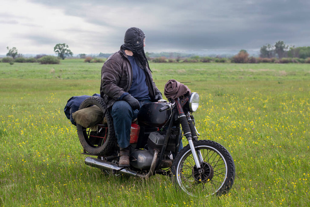 Ein postapokalyptischer Mann auf einem Motorrad auf einer Wiese - Foto, Bild