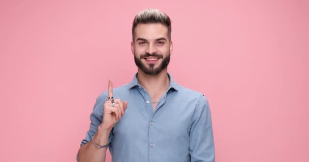 cooler lässiger Mann, der seinen Zeigefinger zeigt, dann herumtanzt und auf rosa Hintergrund herumalbert - Filmmaterial, Video