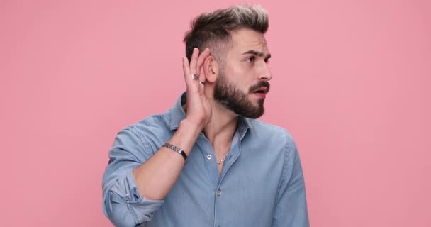 young casual man leaning to hear better but feeling disappointed of the crazy things he heard on pink background - Footage, Video