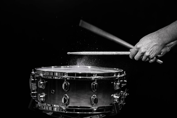 Drum sticks hitting snare drum with splashing water on black background under studio lighting. Black and white. Photo in motion. - Photo, Image